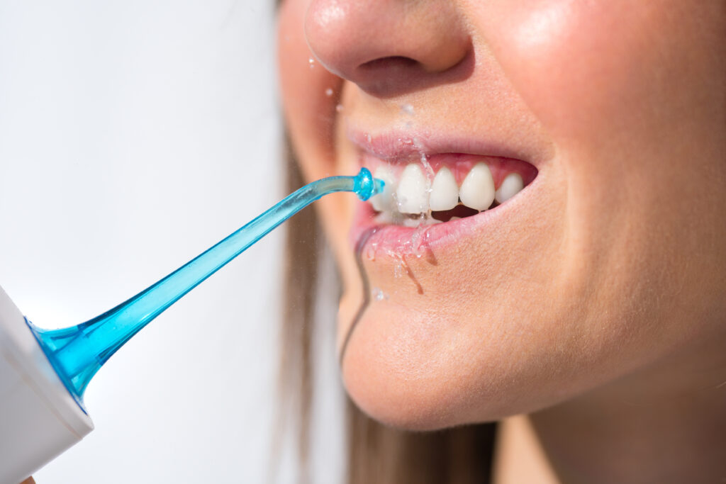 Closeup of woman with perfect smile using water flosser or oral irrigator. High quality photo